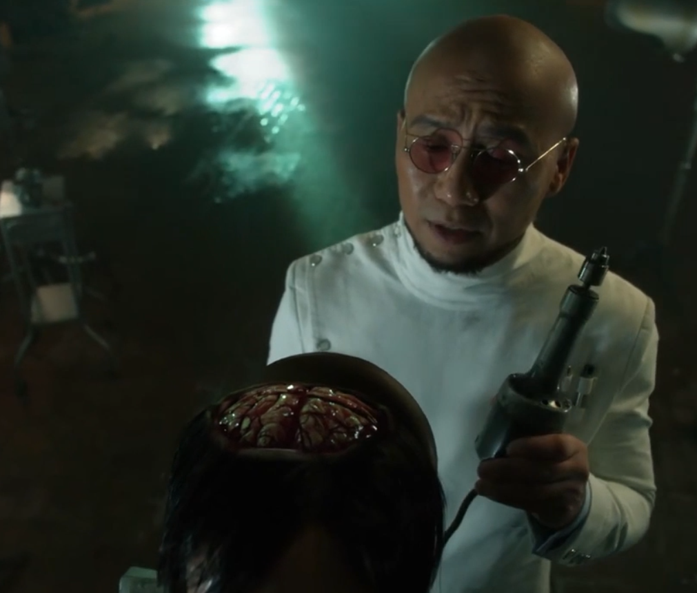Hugo is performing open brain surgery on the Riddler, wielding a scary looking metal implement with an electric charge.